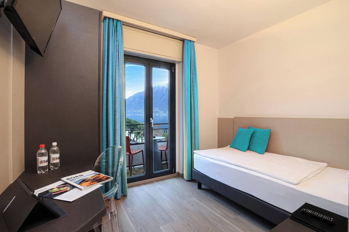 Habitación de hotel con cama, escritorio, silla, computadora portátil y ventana con cortinas.