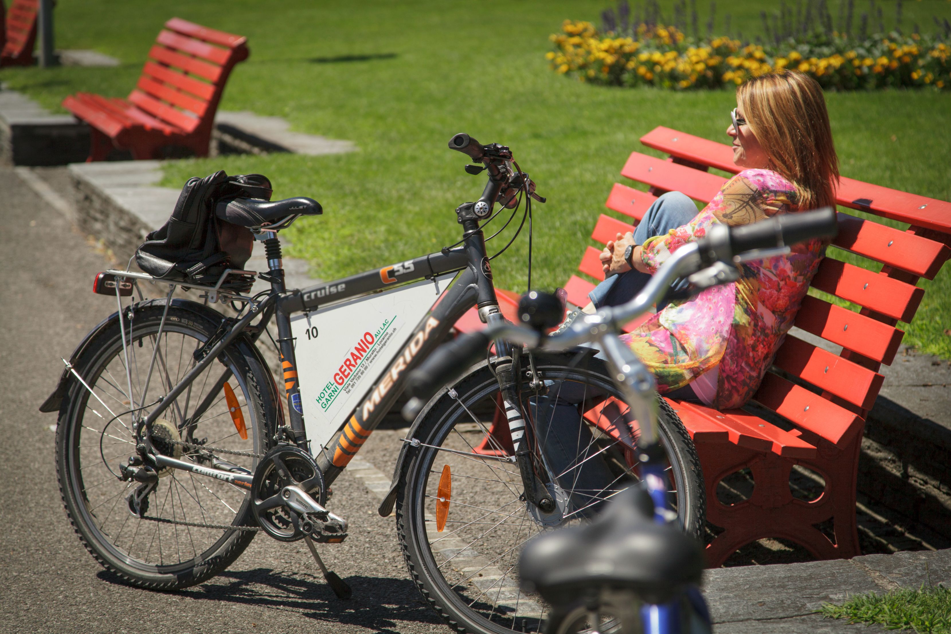 A bicycle parked next to a red bench in a park.