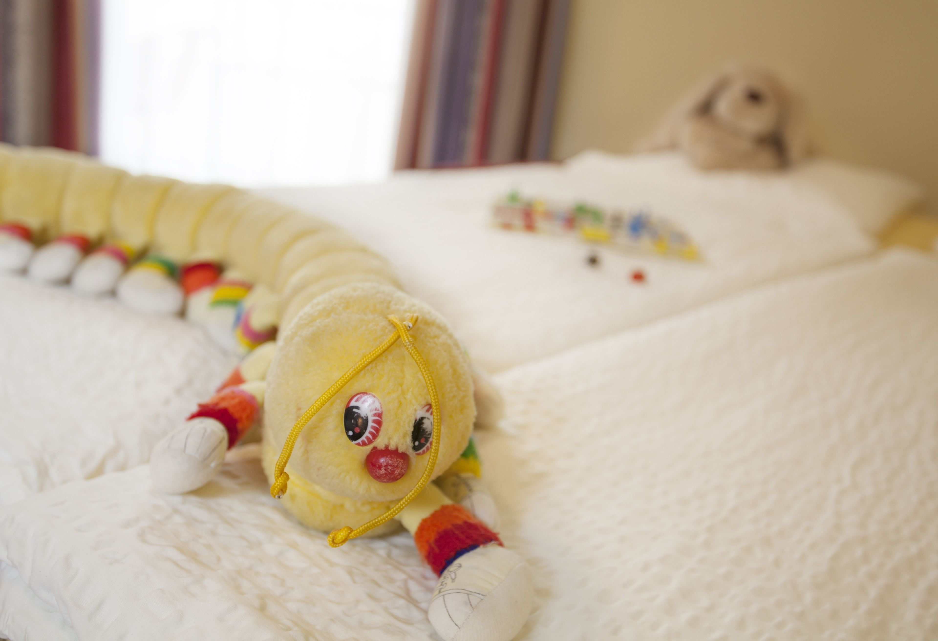 A plush toy on a bed with a white textured blanket.