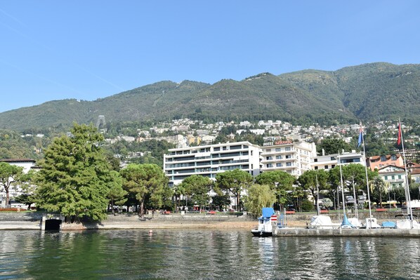 Un hotel frente al agua con varios pisos, un puerto deportivo con barcos y colinas verdes de fondo.