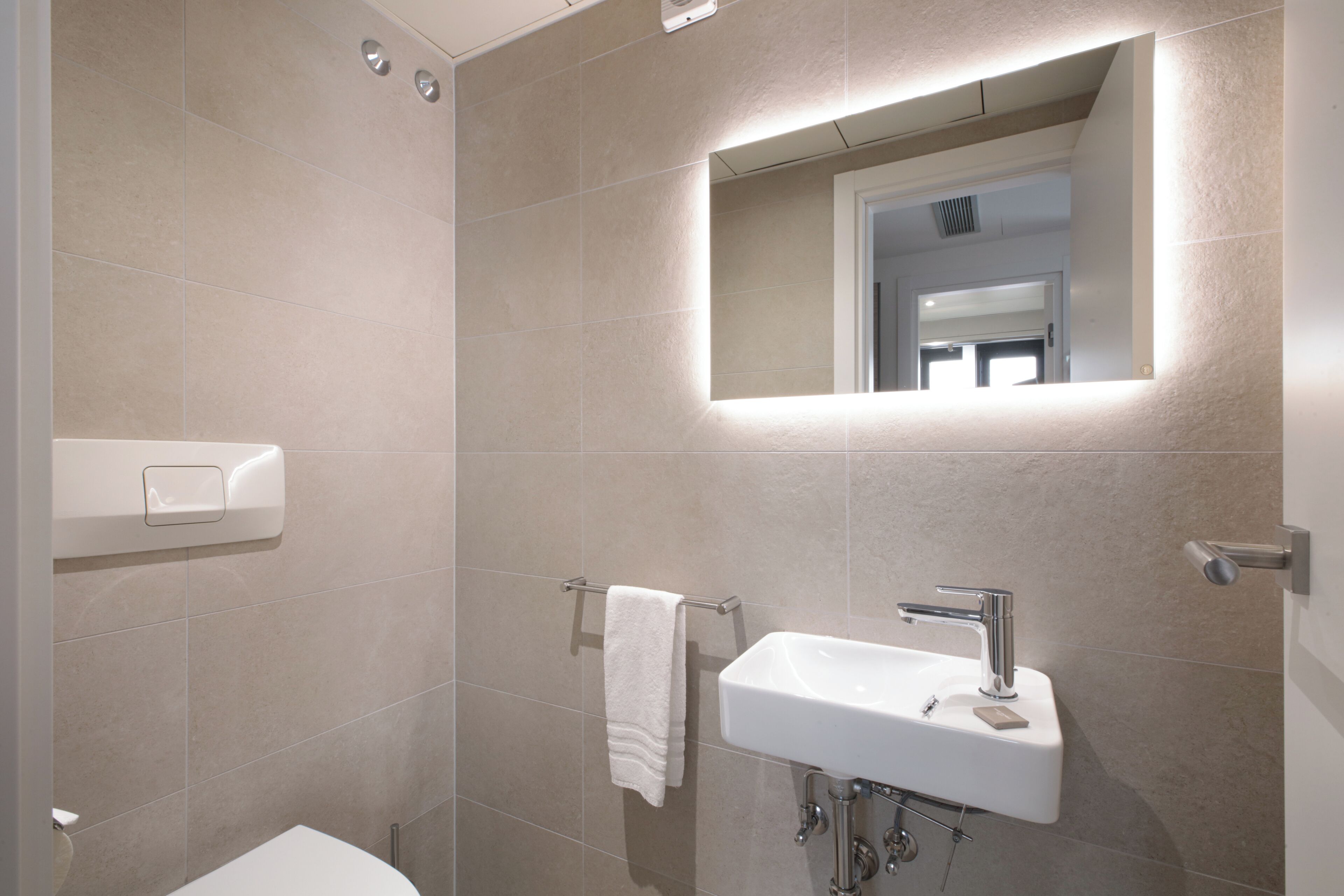 Un baño moderno con un lavamanos blanco, un perchero y un espejo.