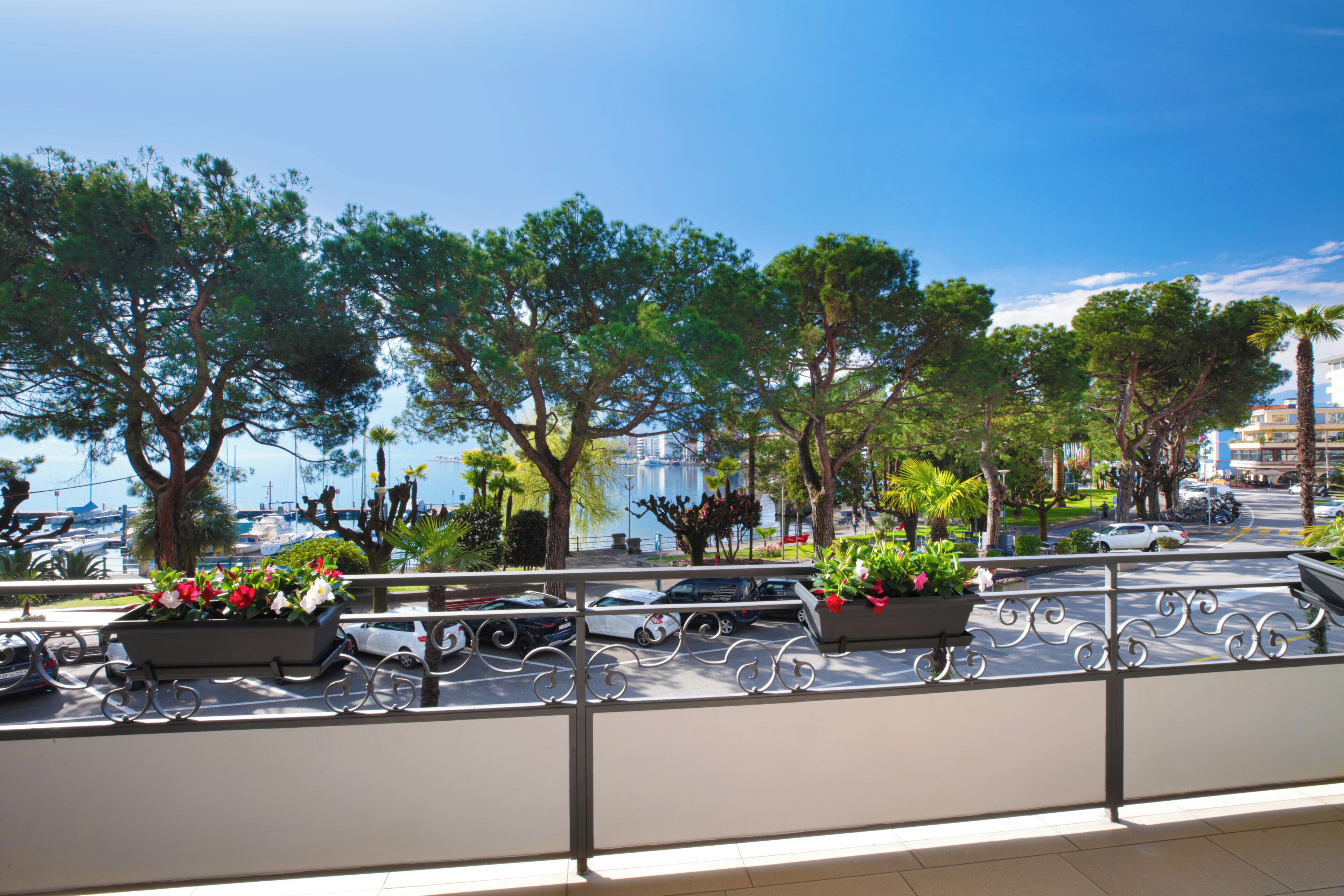A balcony with a railing, potted plants, and a view of the marina and buildings.