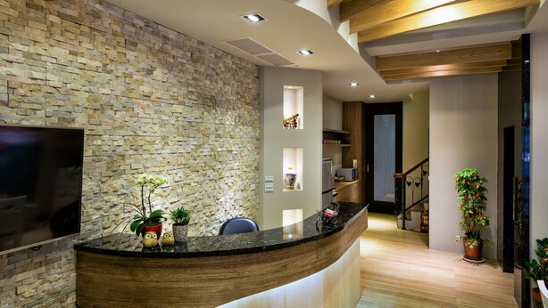 A modern reception area with a stone wall, wooden ceiling beams, and a curved reception desk. - Fun Going B&B (Hualien City)