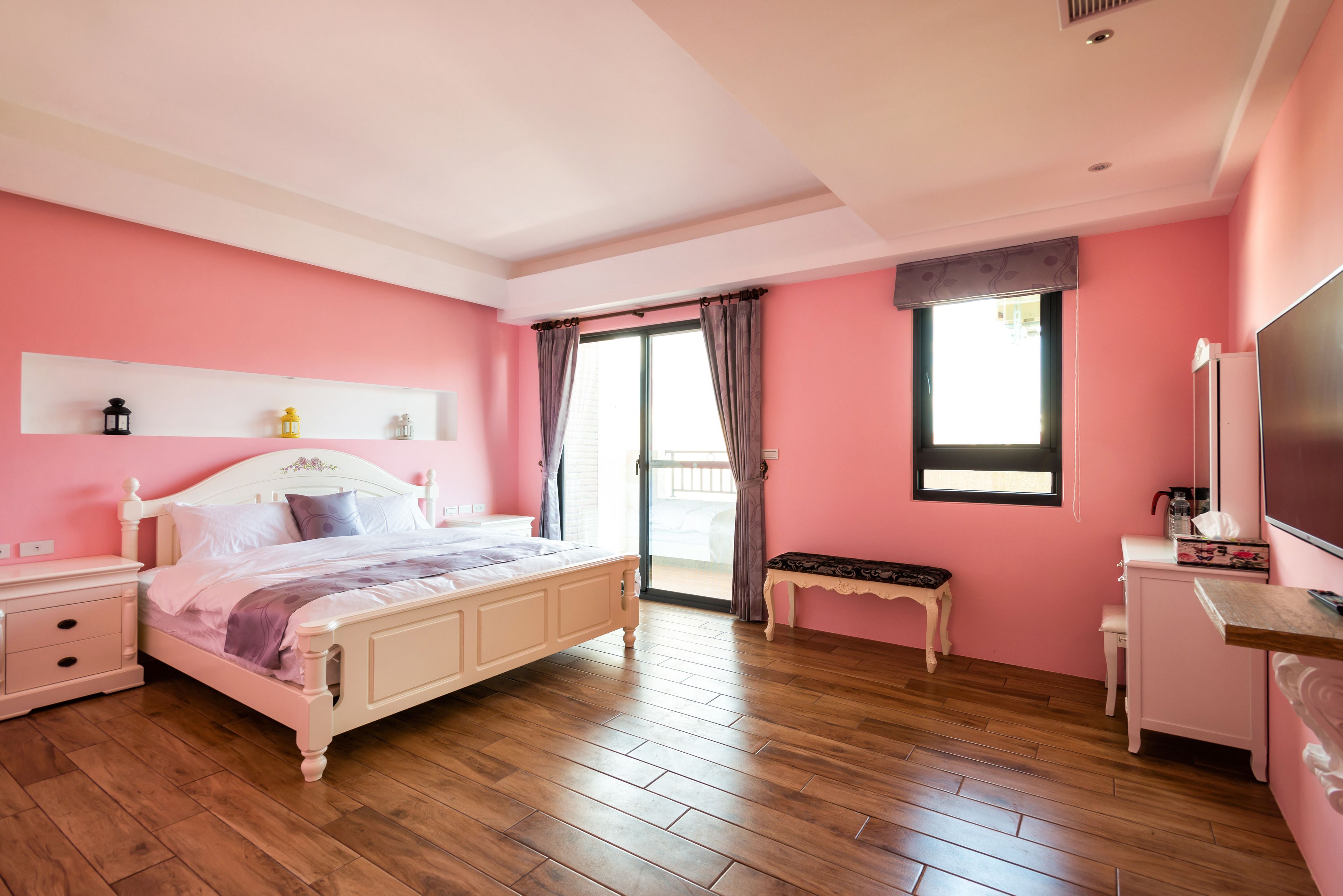 A bedroom with a bed, bedside tables, a bench, a dresser, and a window with curtains.