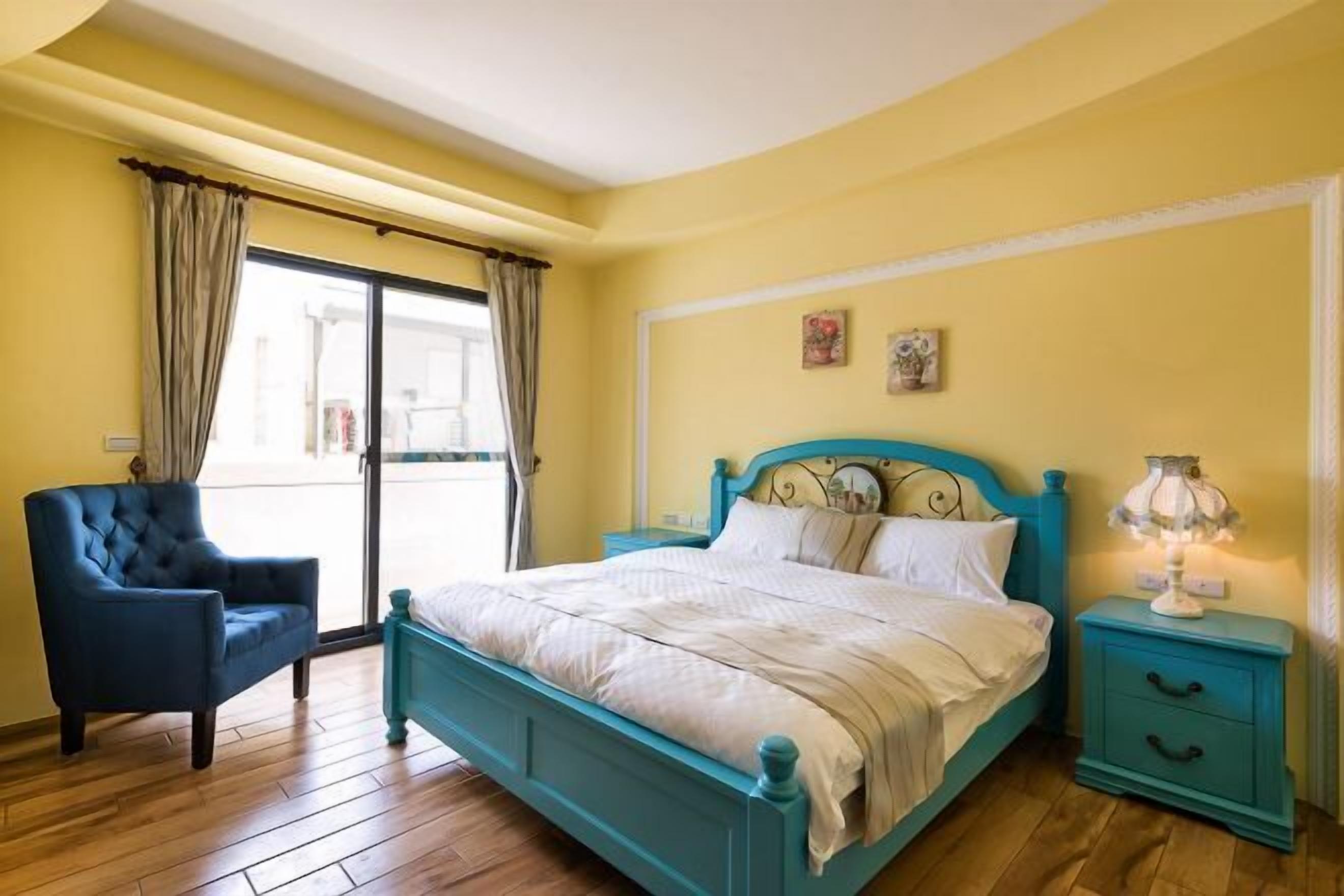 A bedroom with a bed, a chair, a nightstand, and a window with curtains.