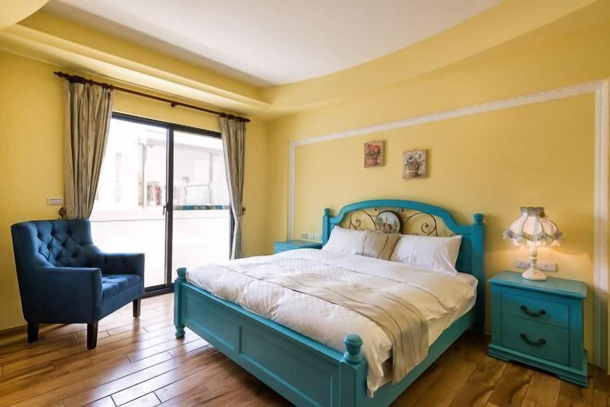 A bedroom with a bed, a chair, a nightstand, and a window with curtains.