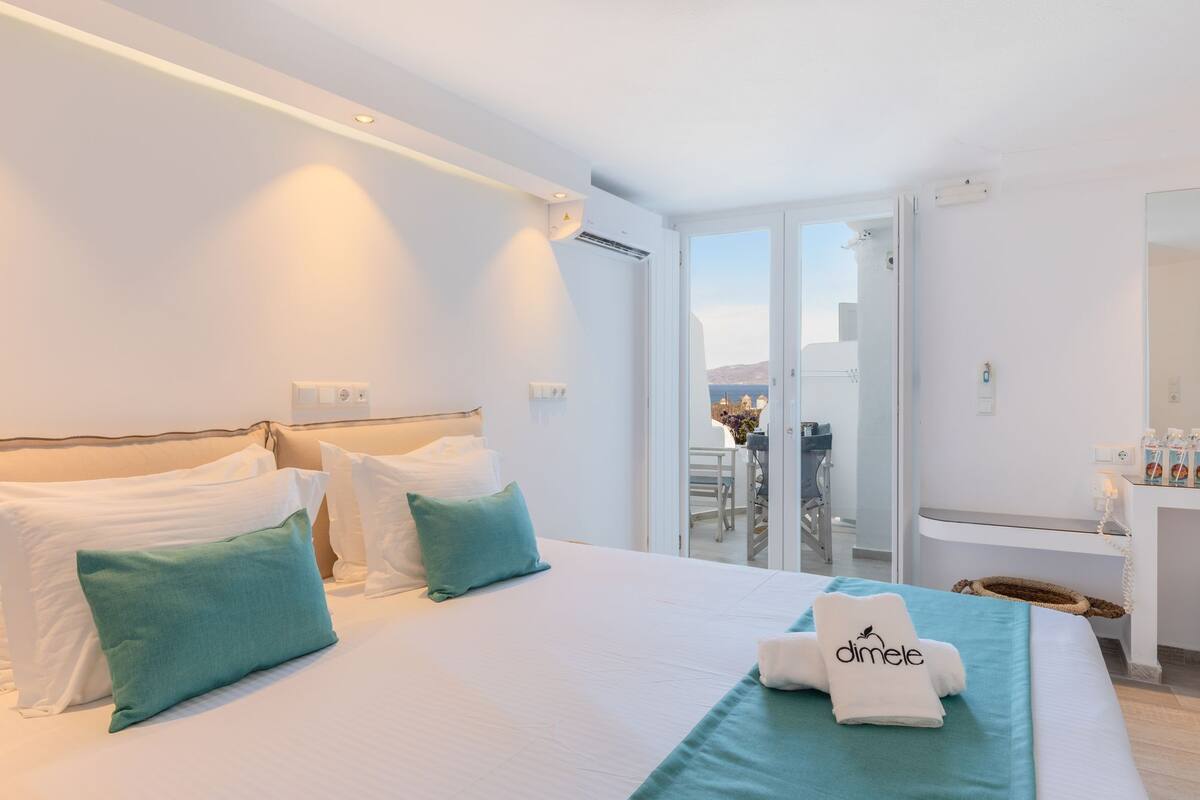A hotel room with a bed, a balcony with a view, a bathroom, and a desk.