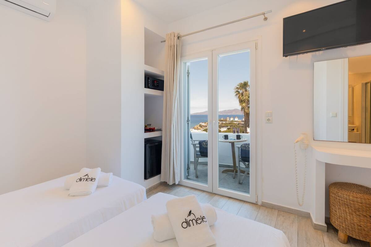 A hotel room with two beds, a TV, a bathroom, and a view of the sea.