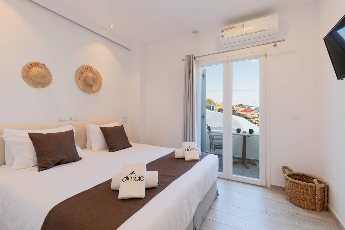 A hotel room with a bed, two hats on the wall, a TV, and a balcony with a view.