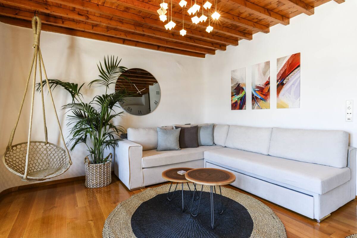 A modern living room with a white sofa, a hanging plant, a round mirror, and abstract art on the wall.
