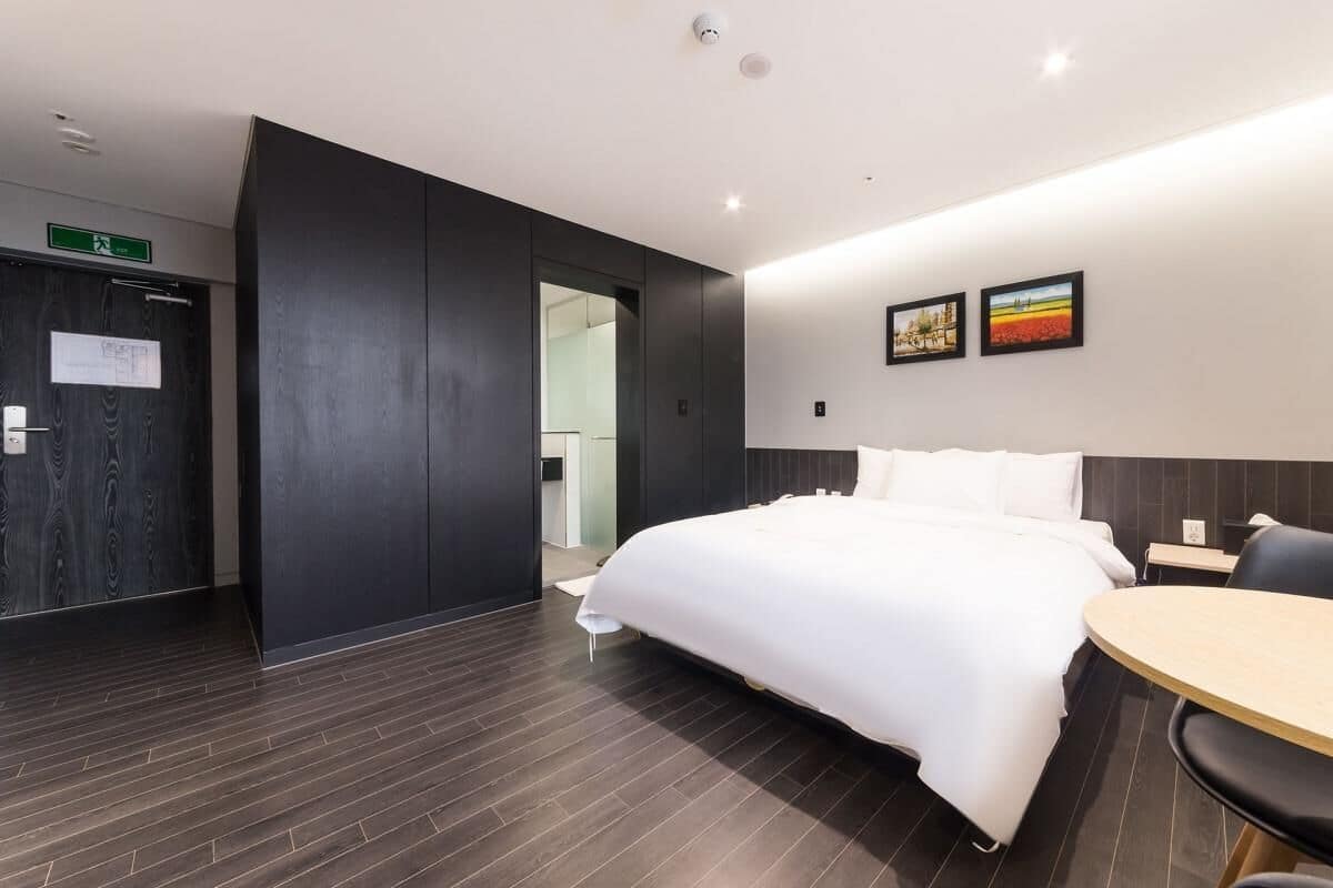 A modern hotel room with a large bed, a small round table, and a dark wooden floor.