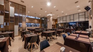 Un restaurante moderno con varias mesas y sillas, una zona de bar y un amplio ventanal que proporciona luz natural.