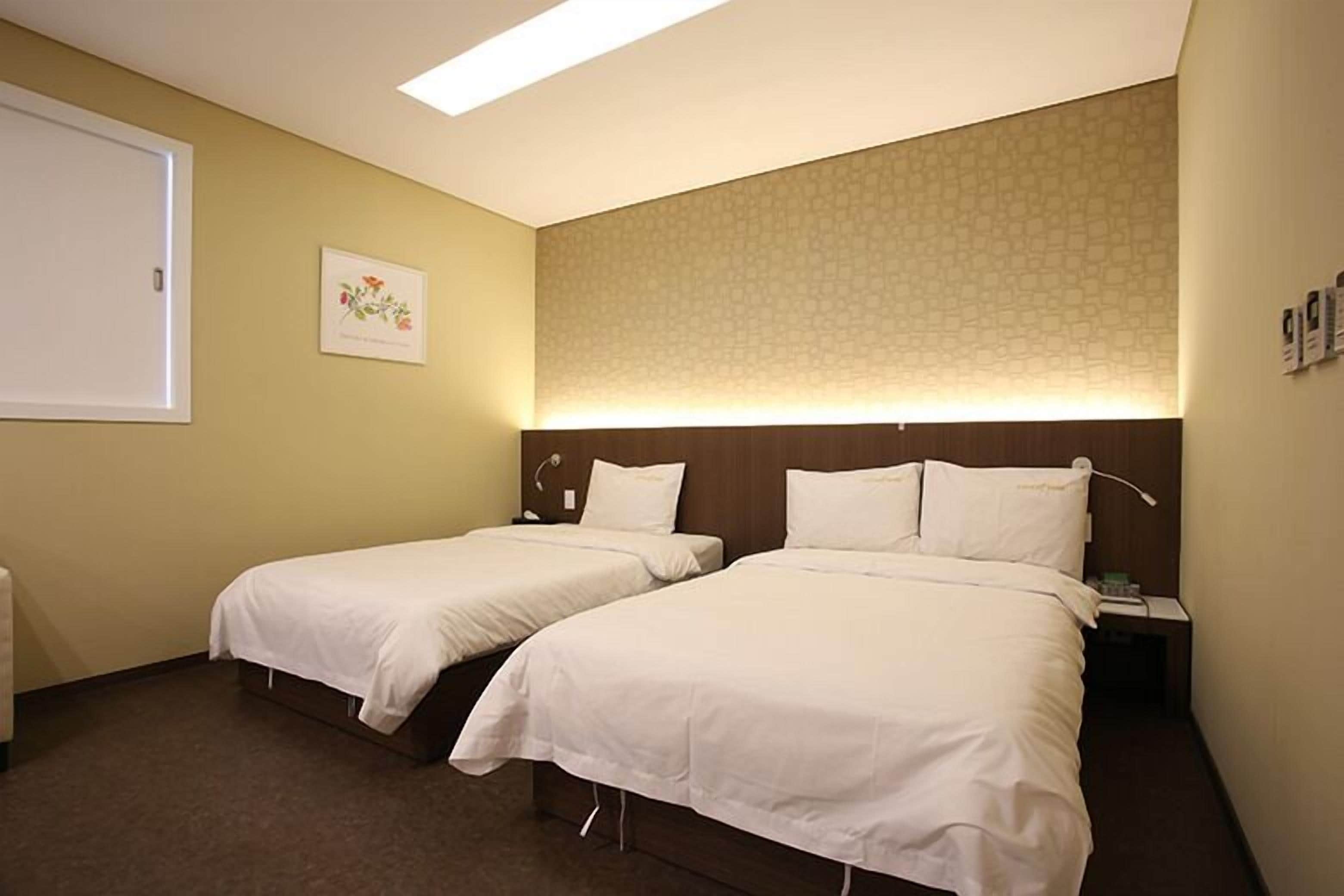 Habitación de hotel con dos camas individuales, una mesita de noche con lámpara, una obra de arte en la pared y un cabecero estampado.