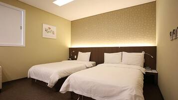 Habitación de hotel con dos camas individuales, una mesita de noche con lámpara, una obra de arte en la pared y un cabecero estampado.