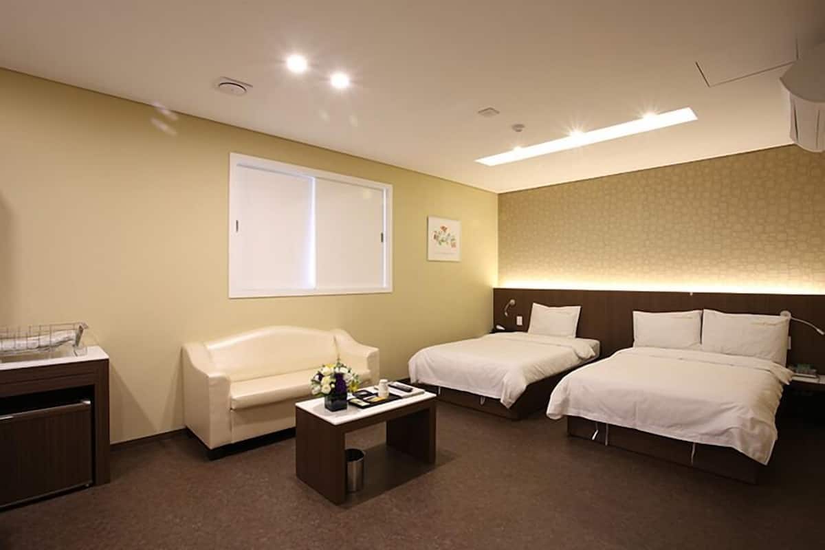A hotel room with two beds, a sofa, a small table, and a window.