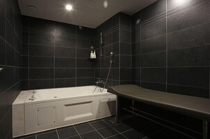 Un baño moderno con una bañera independiente, un banco y paredes de baldosas oscuras.