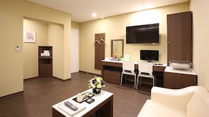 Habitación de hotel con escritorio, televisor, silla, sofá y una mesita con un jarrón de flores.