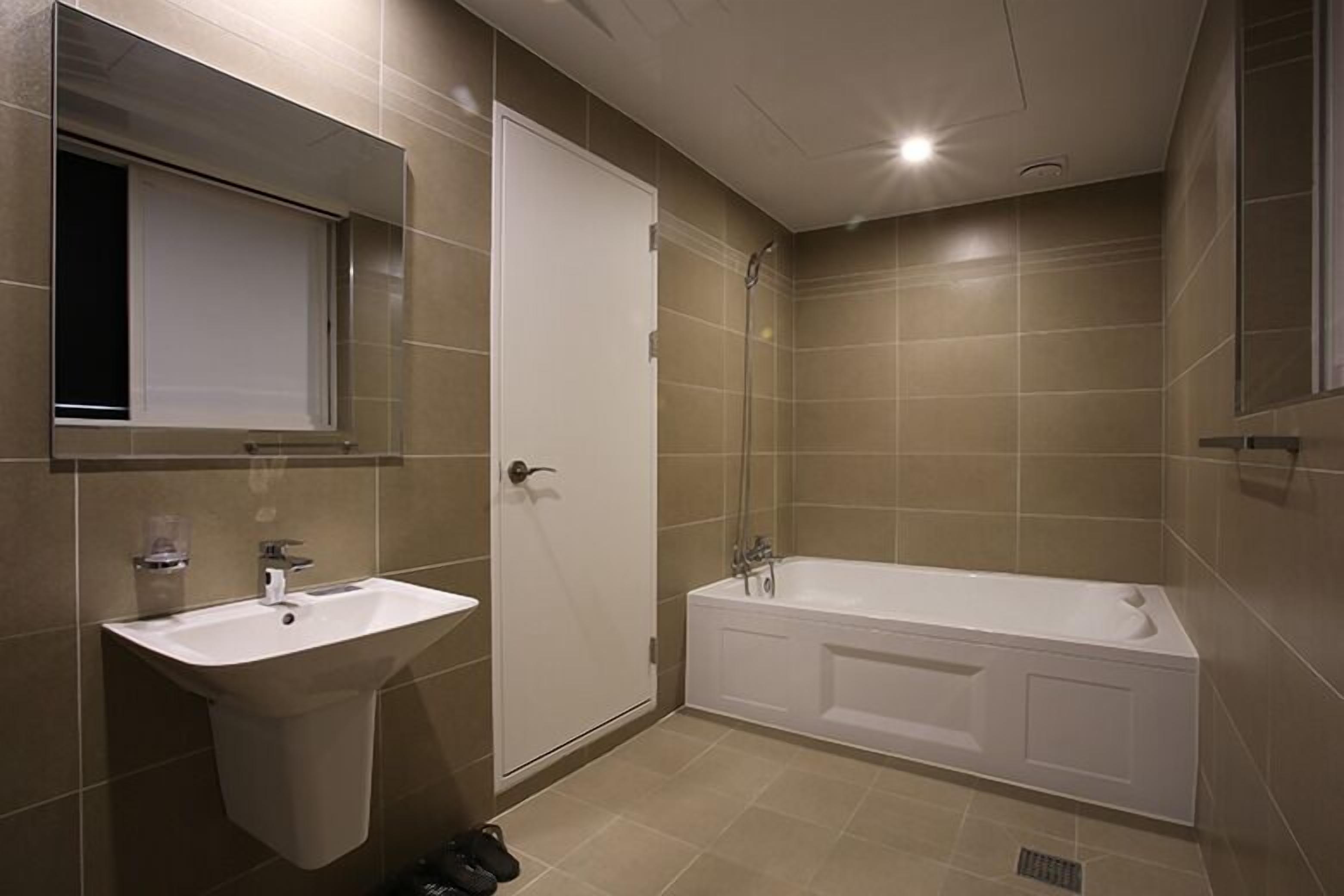 A modern bathroom with a sink, mirror, door, and bathtub.