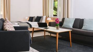 Una habitación de hotel moderna con una cama, un sofá, una mesita con un ordenador portátil y una planta en maceta.