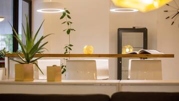 Un espace d’attente moderne avec un comptoir d’accueil en bois, des chaises blanches et une grande plante en pot.