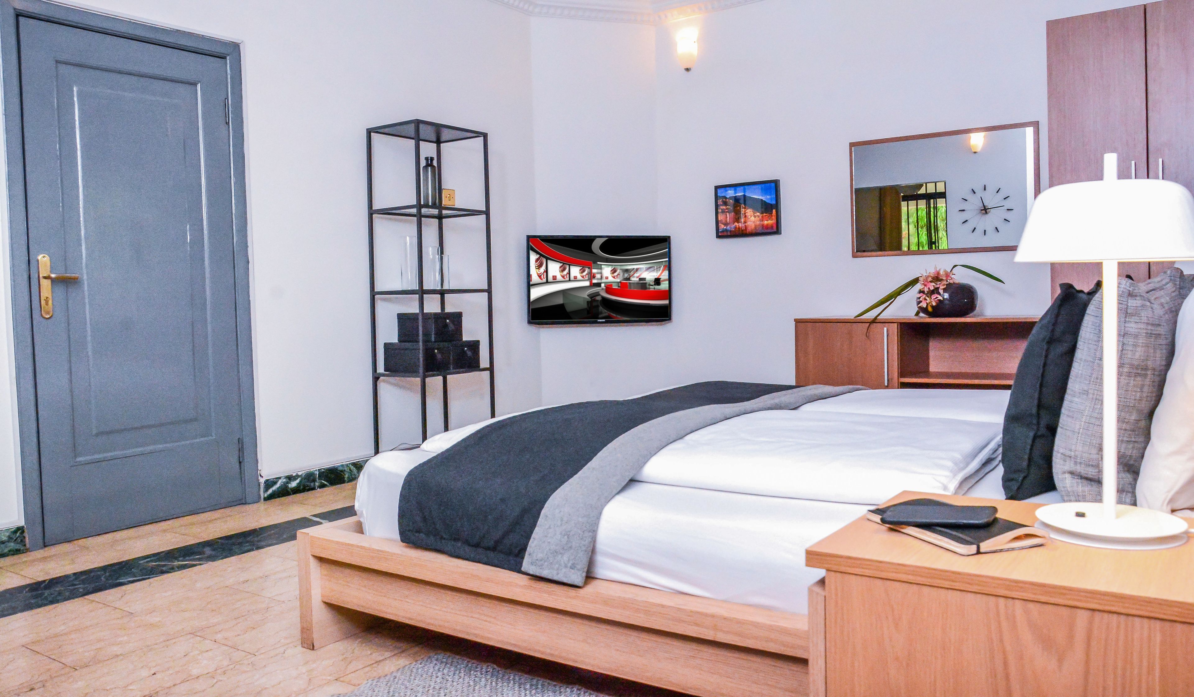 A modern bedroom with a bed, bedside table, lamp, shelf, and artwork.