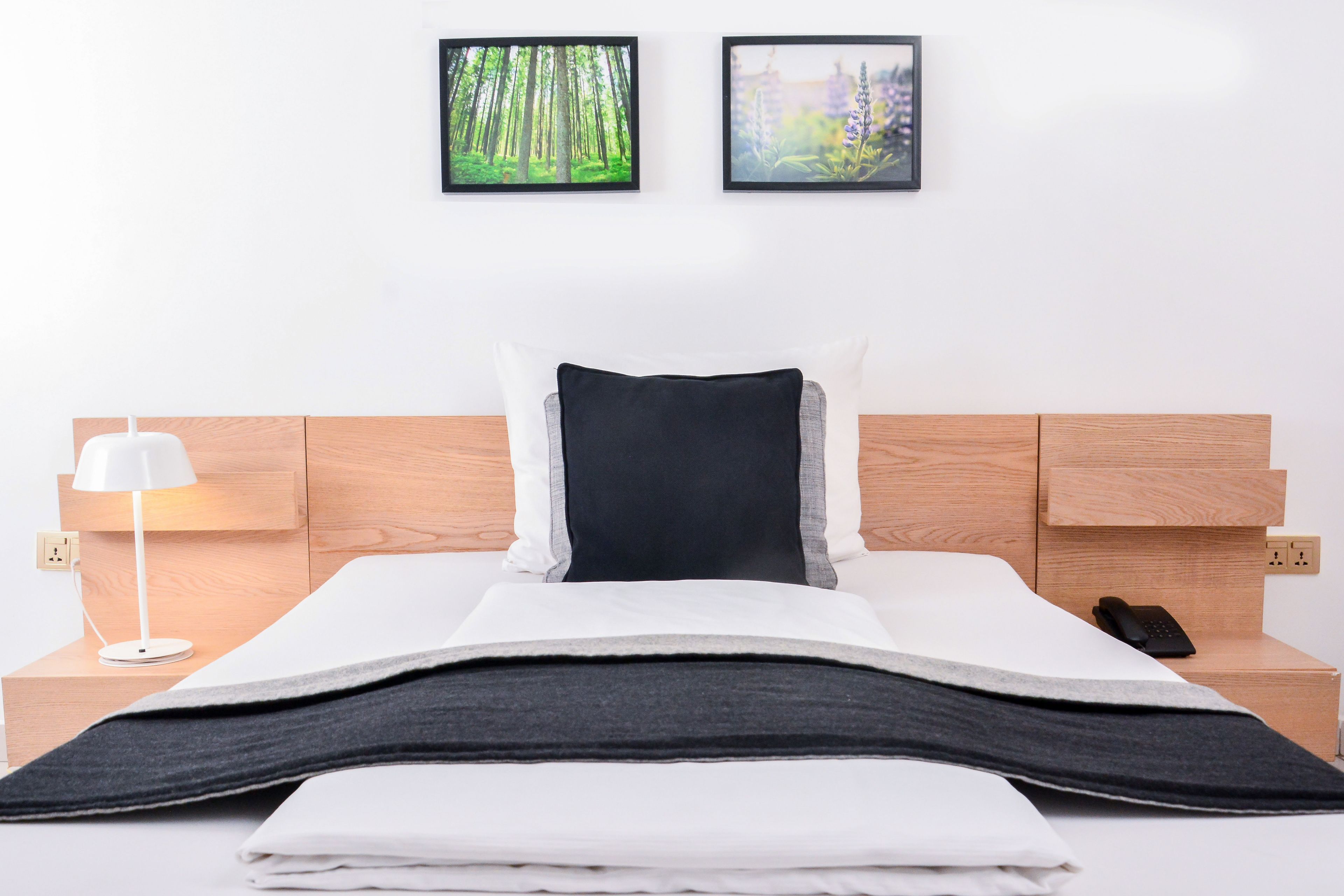 A neatly made bed with a black and white pillow, a white lamp on the nightstand, and two framed pictures on the wall.