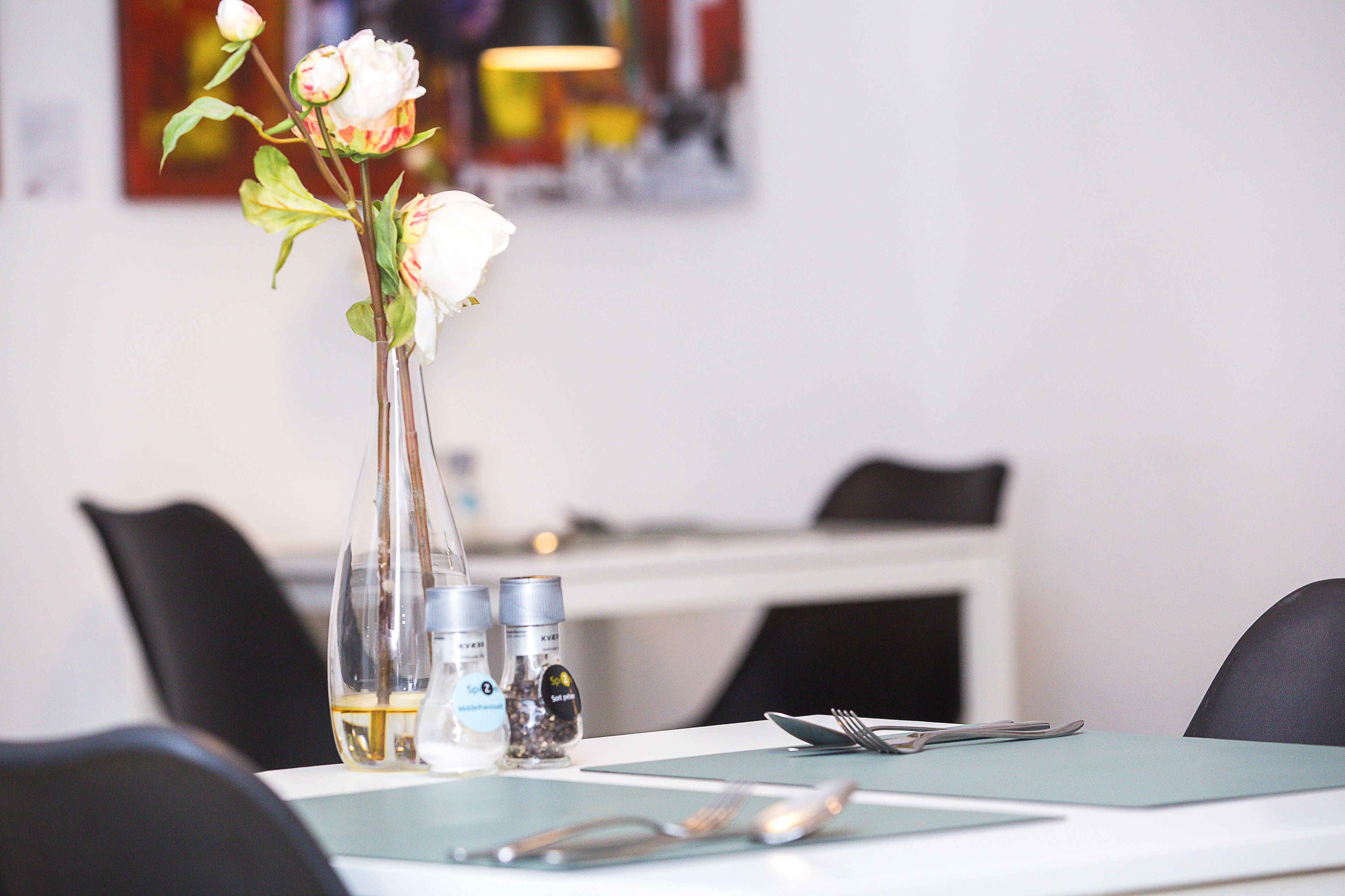 Una mesa de comedor con un florero, saleros, pimenteros y una botella de agua.