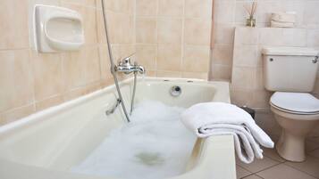A bathroom with a bathtub, toilet, and a soap dispenser on the wall.