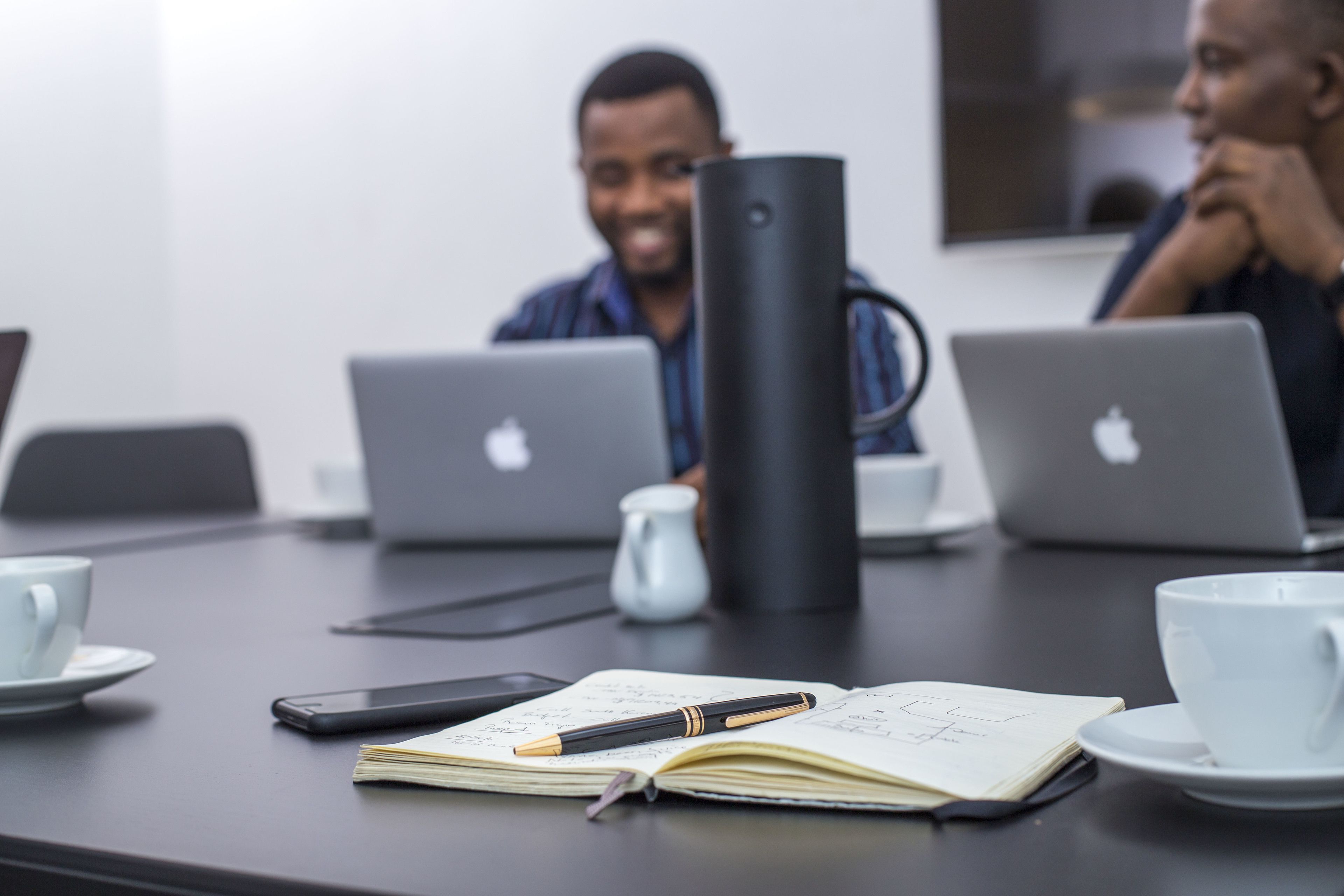 A conference table with laptops, a coffee cup, a notebook, and a pen.