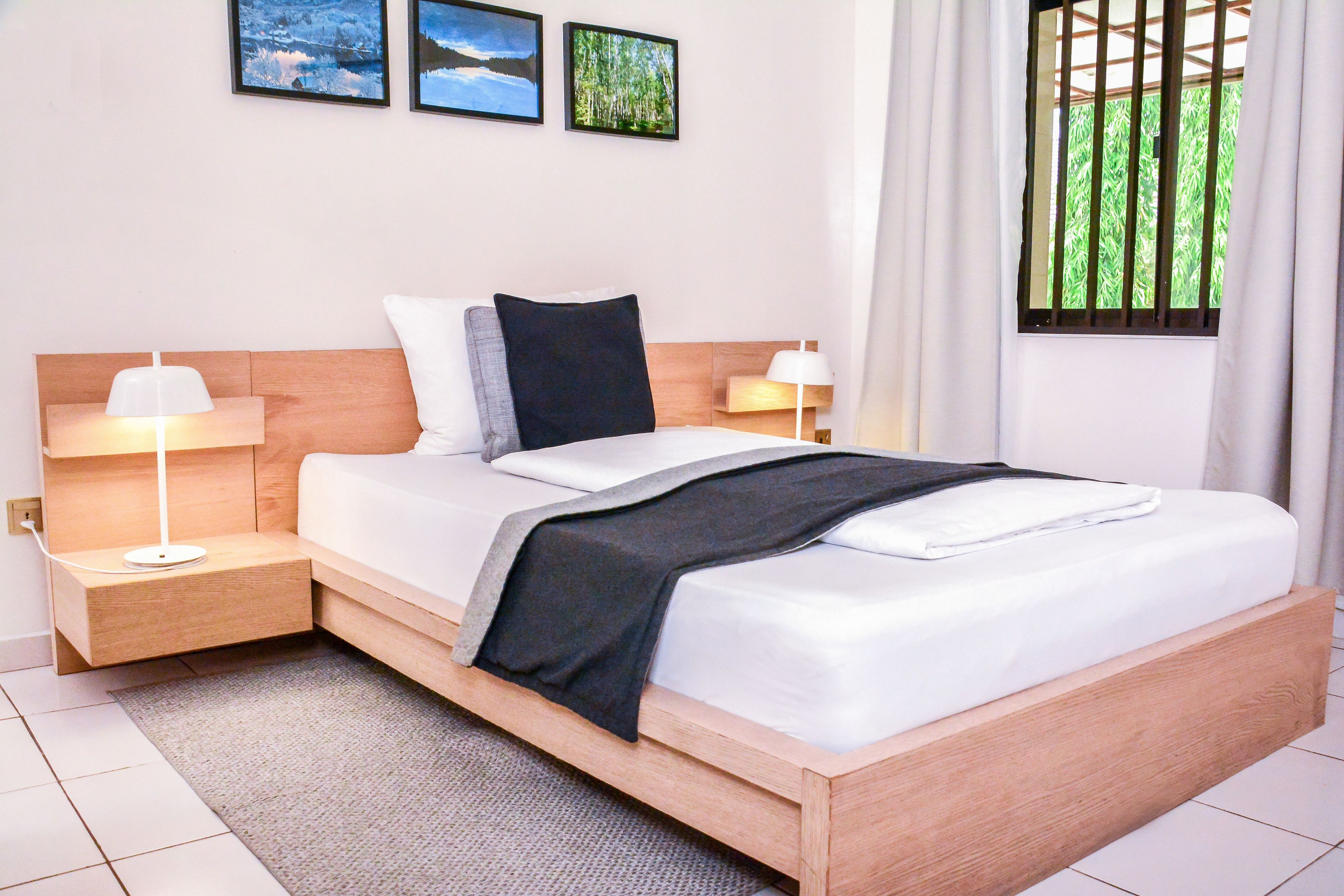 A modern hotel room with a wooden bed, white bedding, two bedside tables with lamps, and framed pictures on the wall.