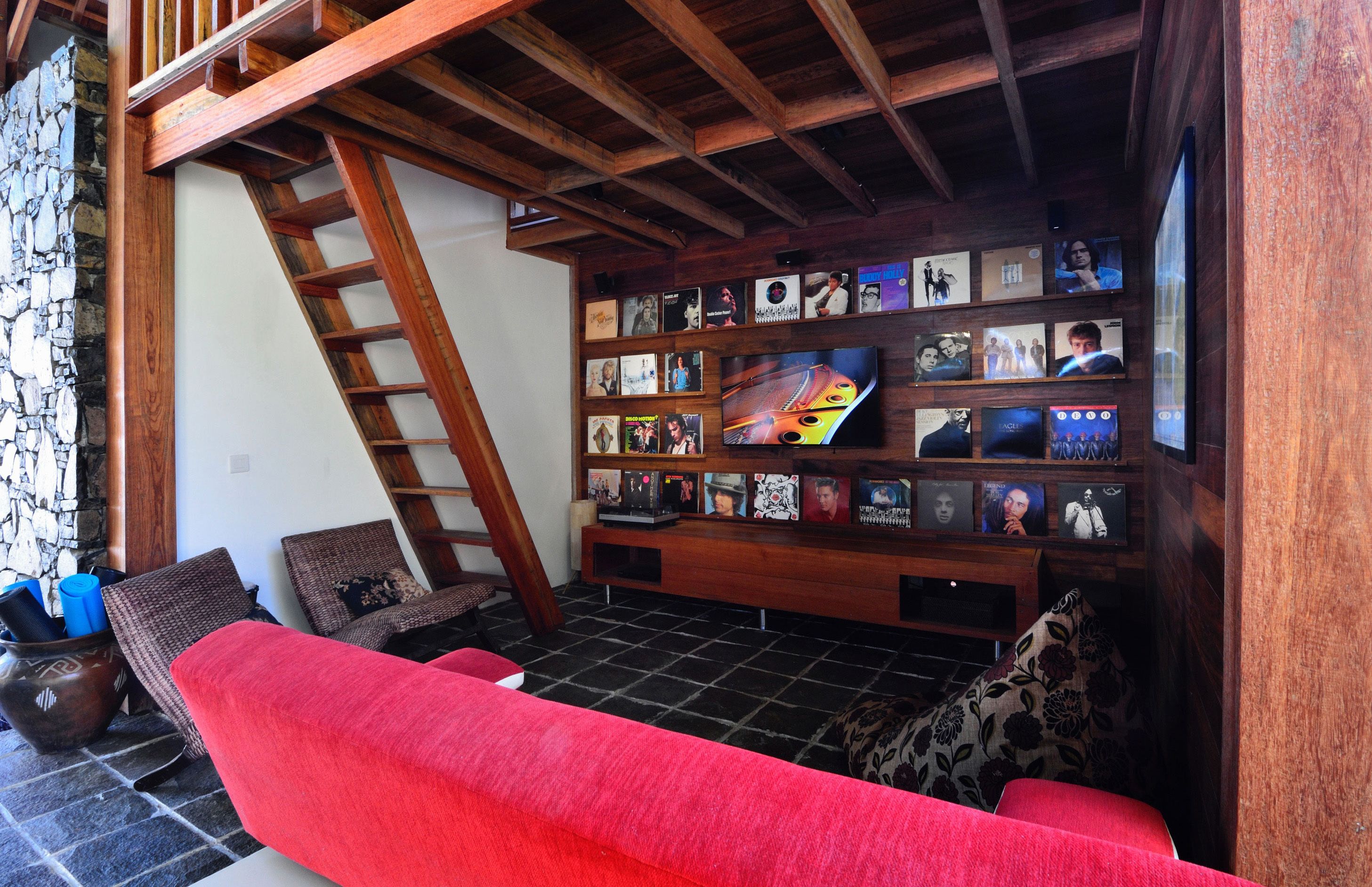 Un espacio de sala acogedor con un sofá rojo, un mueble de entretenimiento de madera con fotos enmarcadas y una pared de piedra.