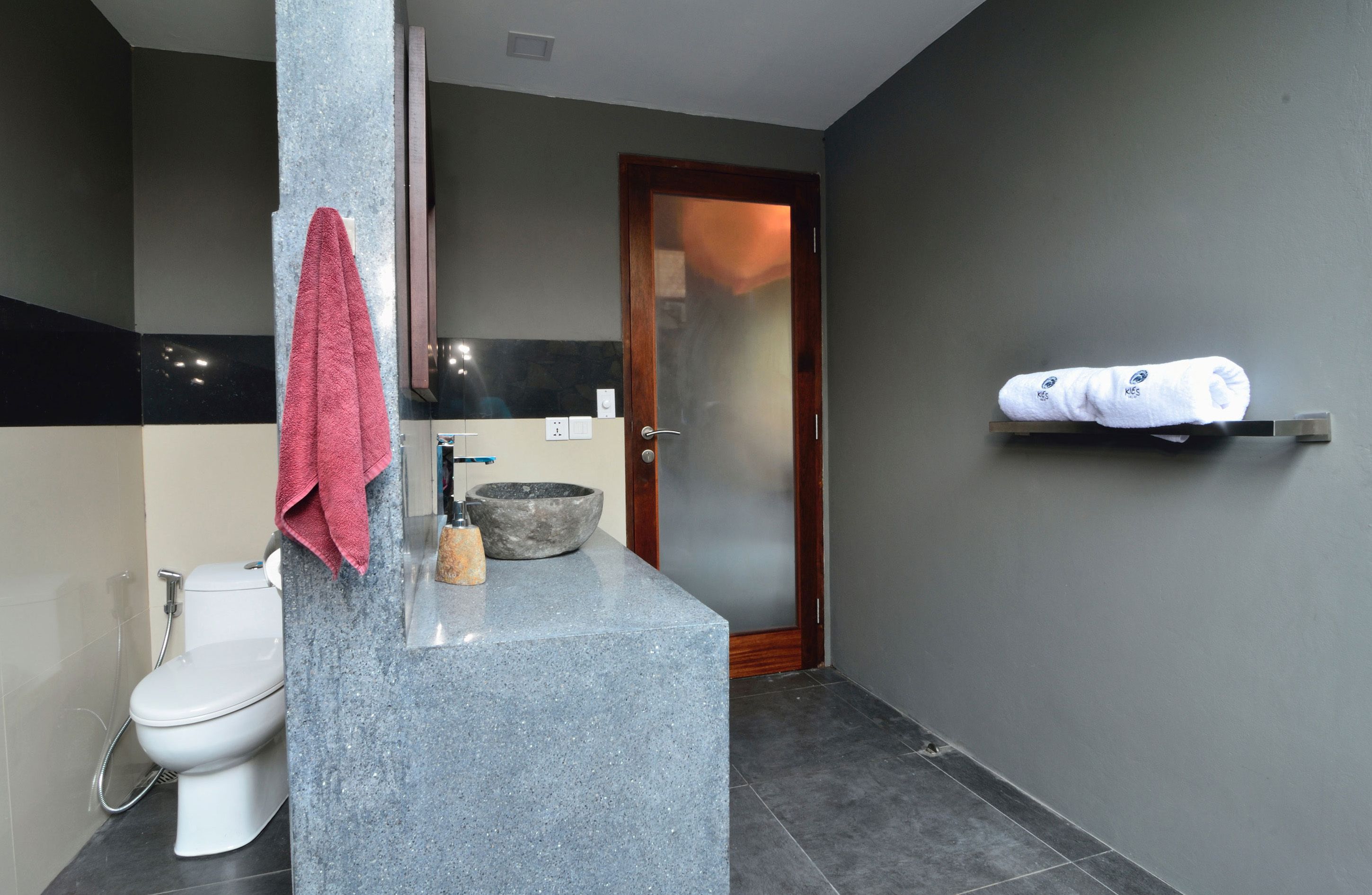 Et moderne badeværelse med bordplade i granit, et hvidt toilet, en stor vask og en håndklæderække.