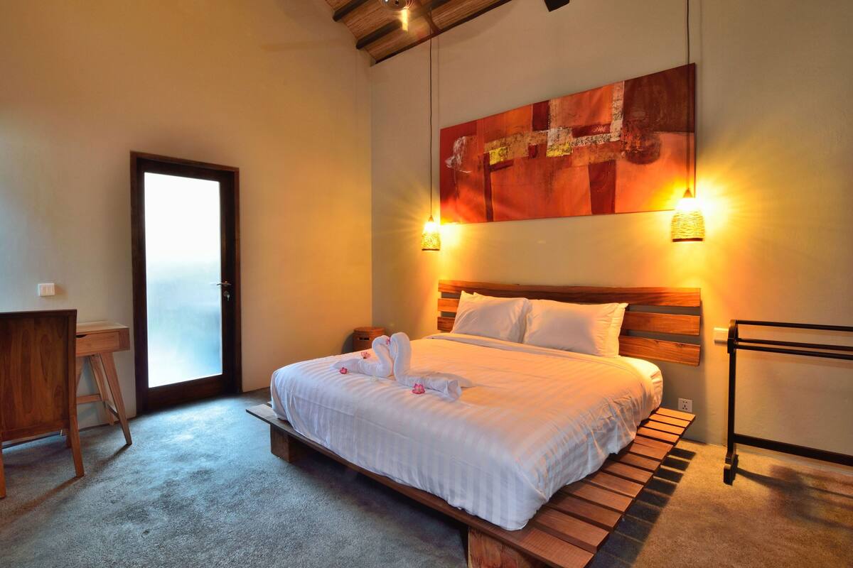 Un dormitorio con una cama de madera, un escritorio y un cuadro abstracto grande en la pared.