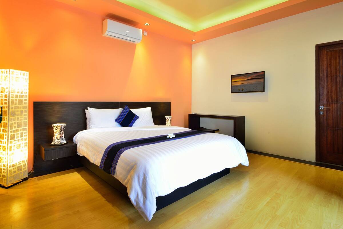 Un dormitorio con una cama, mesitas de noche, aire acondicionado de pared y una puerta de madera.