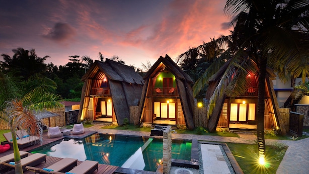 Um resort com duas cabanas de telhado de palha, piscina e espreguiçadeiras.