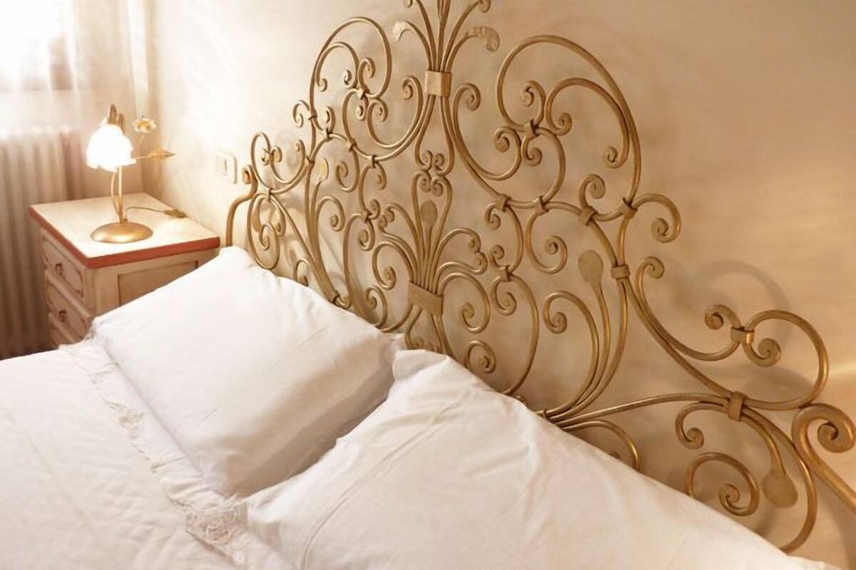 Un lit doté d’une tête de lit décorative en métal, d’une lampe de chevet et d’une table de chevet avec un tiroir.