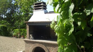 Een bakoven van baksteen buiten, met schoorsteen, omringd door begroeiing.