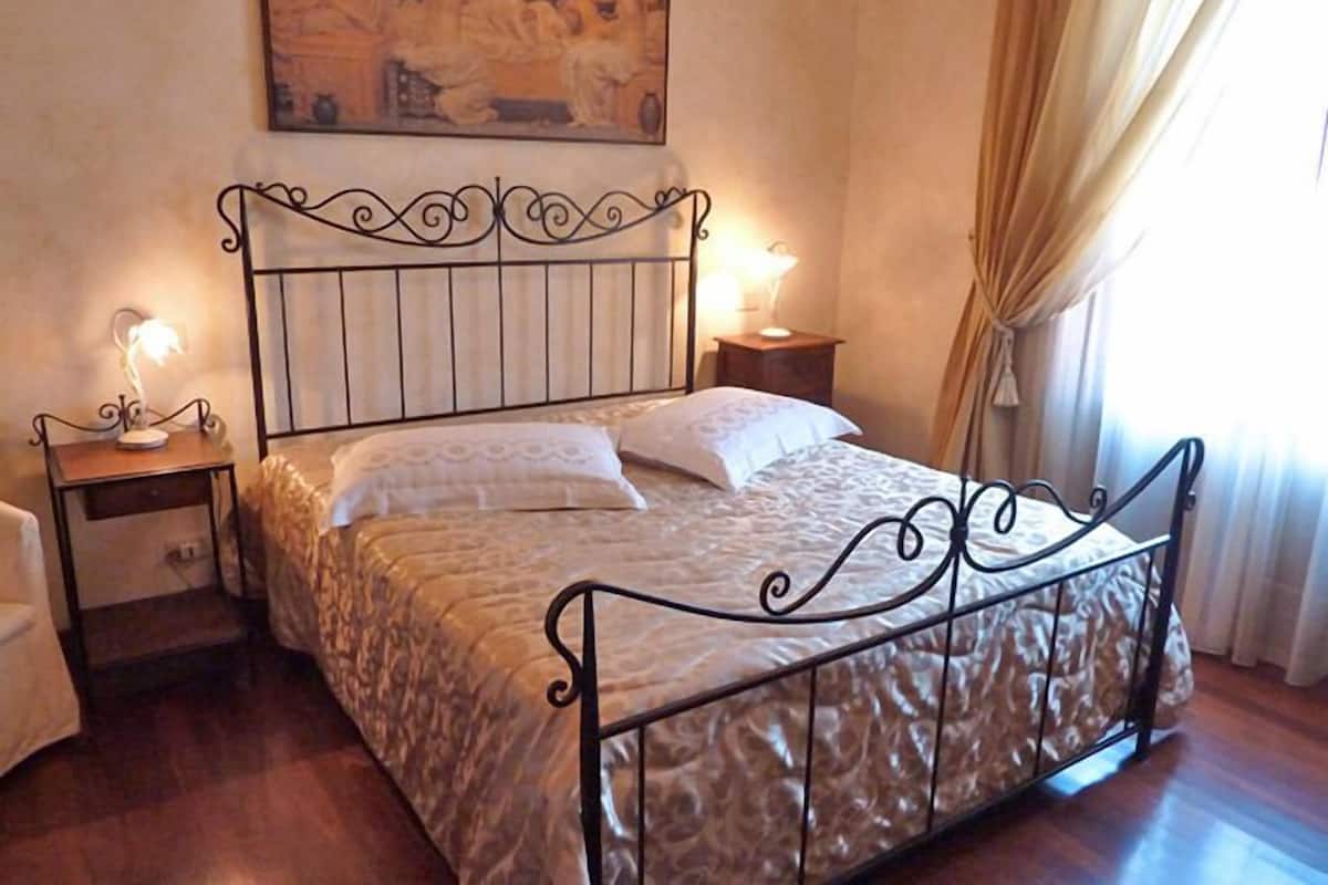 Une chambre à coucher avec un lit à ossature métallique, deux tables de chevet, une commode et un tableau accroché au mur.