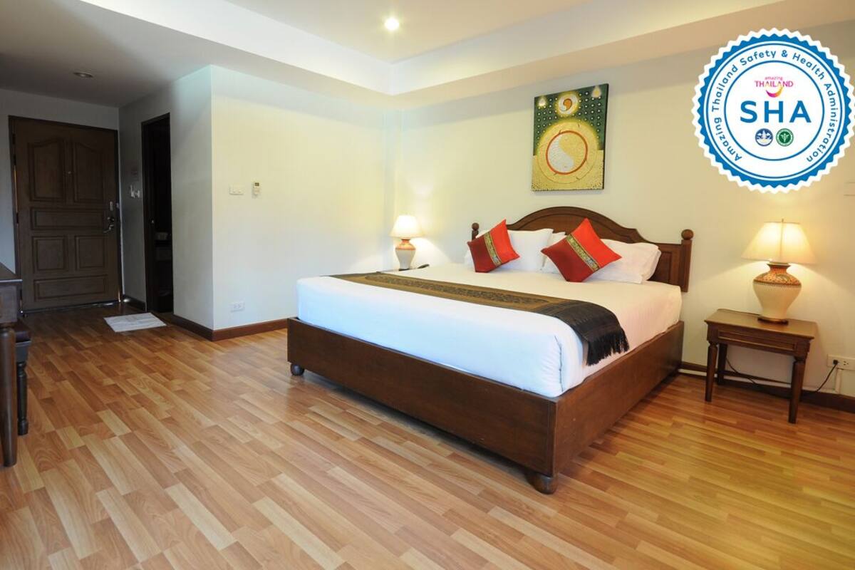 A hotel room with a wooden floor, a bed with pillows, a desk, and a wall-mounted artwork.