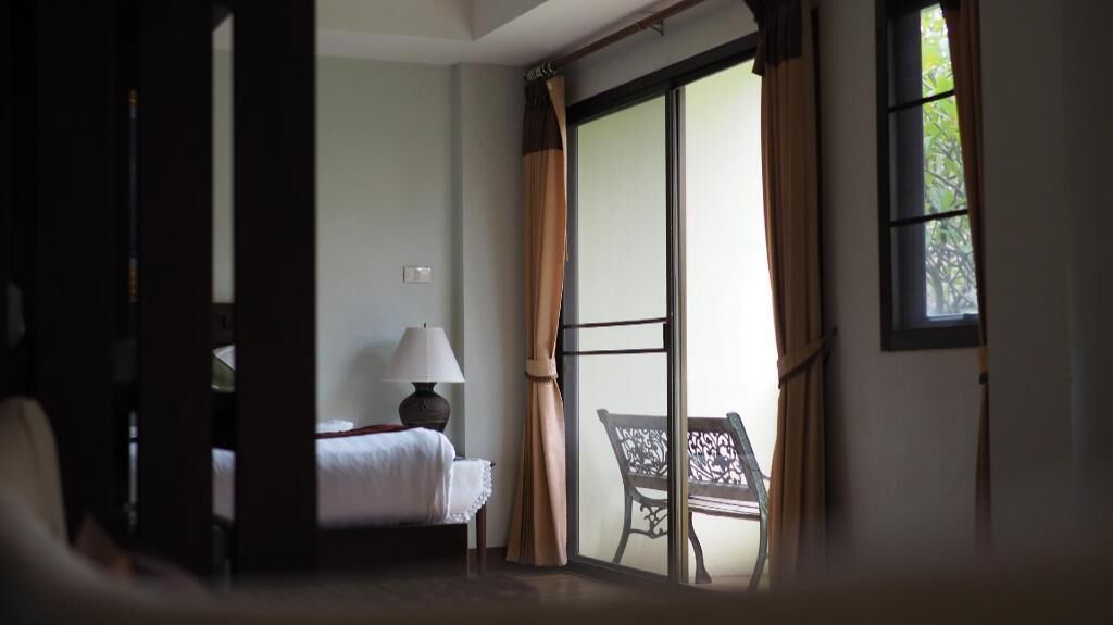 A hotel room with a bed, a chair, a lamp, and a view through a sliding door.