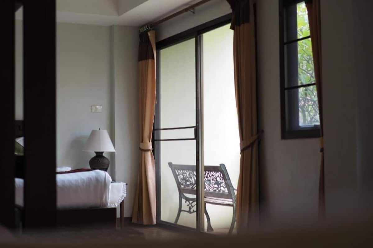 A hotel room with a bed, a chair, a lamp, and a view through a sliding door.