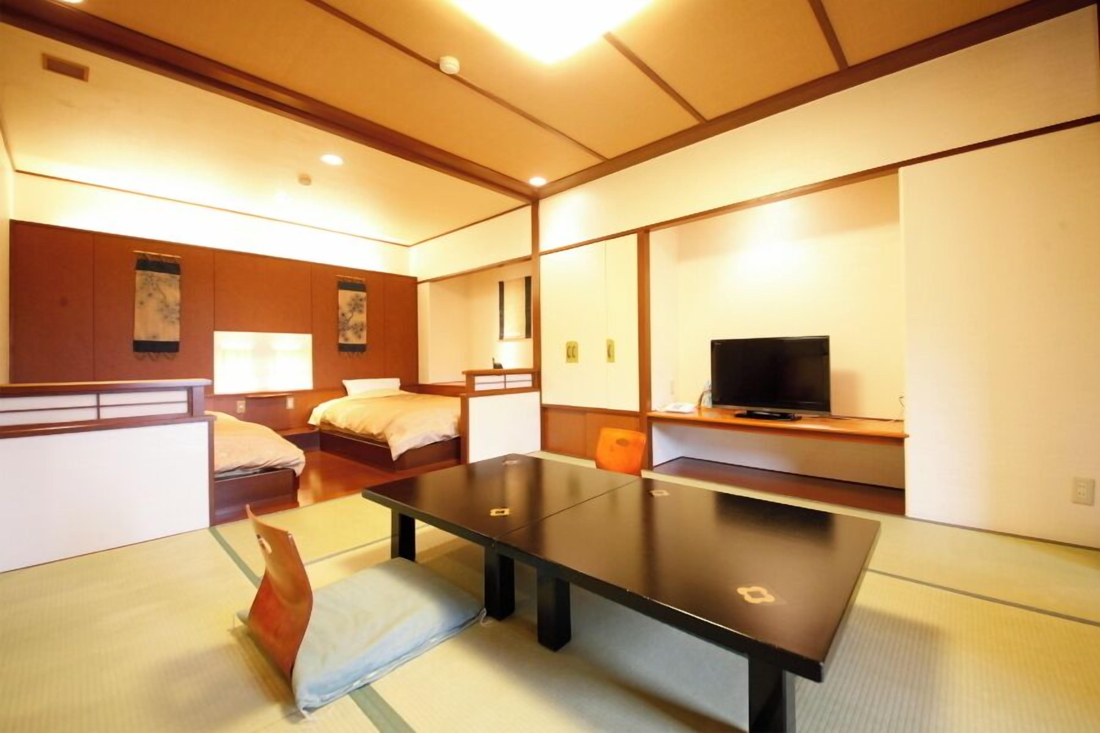 Ein Hotelzimmer mit Tatami-Boden, einem Bett, einem Schreibtisch, einem Fernseher und einem Fenster.