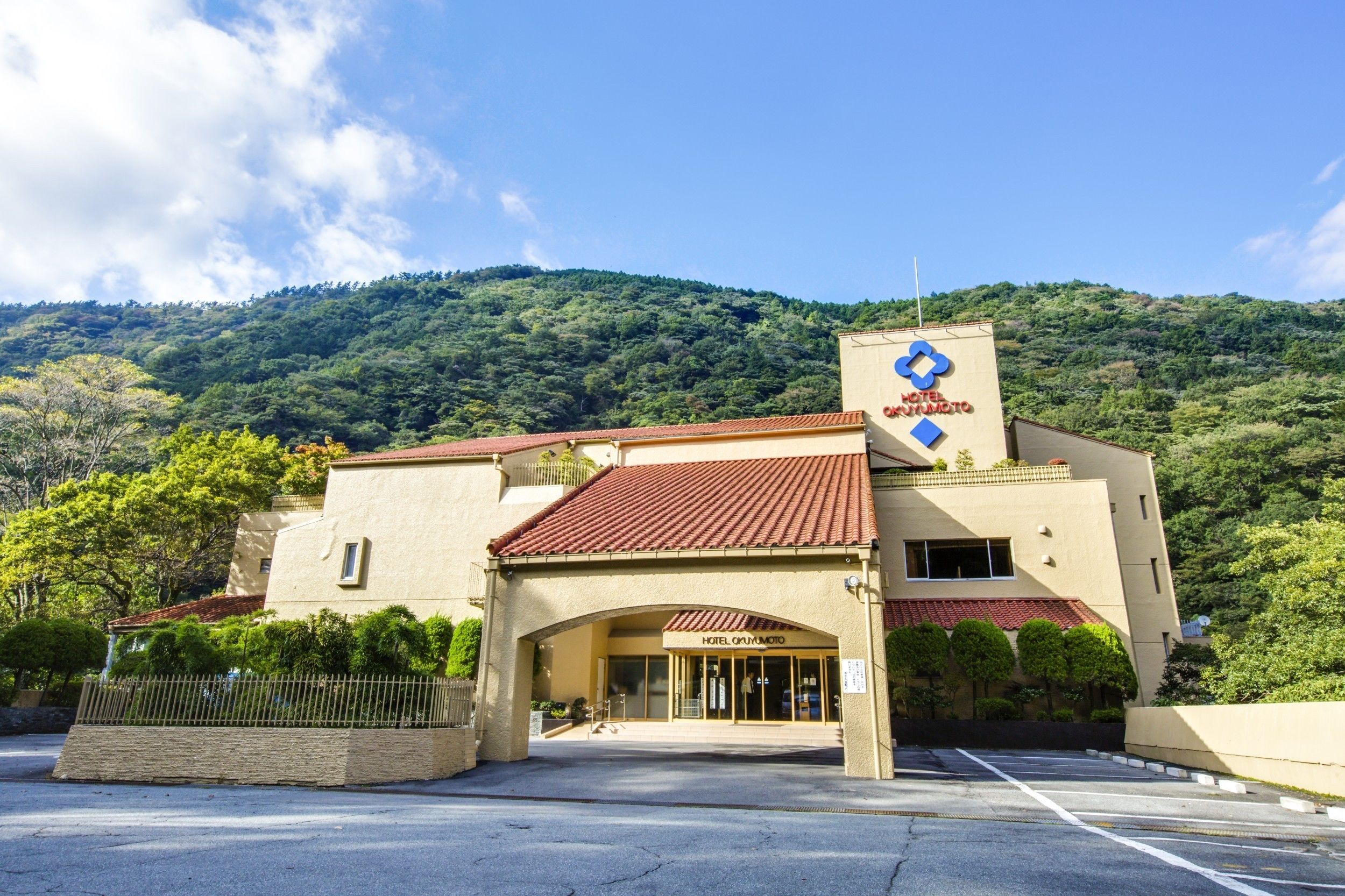 A hotel with a red-tiled roof, a prominent blue logo, and a mountainous backdrop.