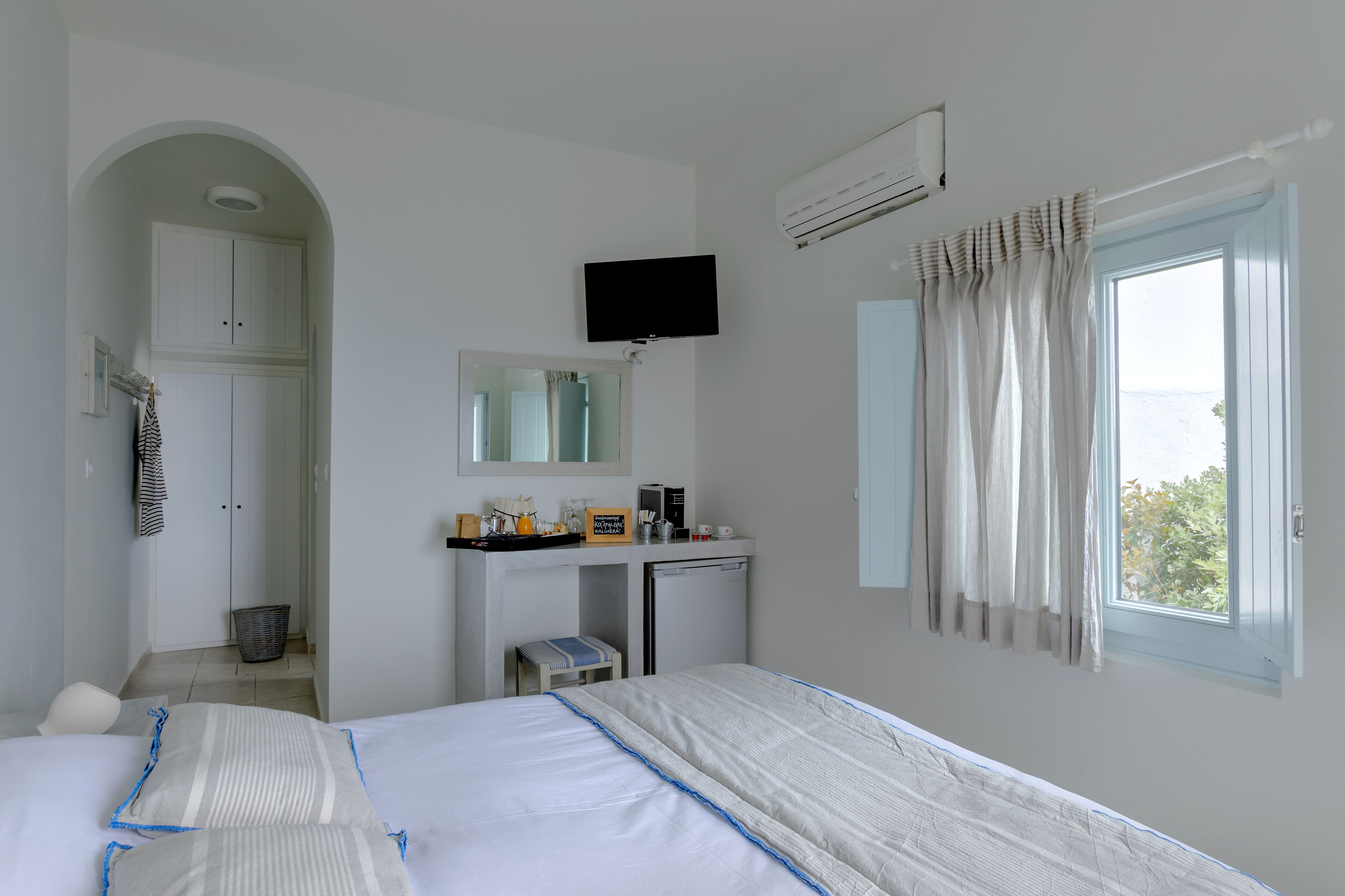 A hotel room with a bed, a desk with a computer, a television, an air conditioner, a window with curtains, and a wardrobe.