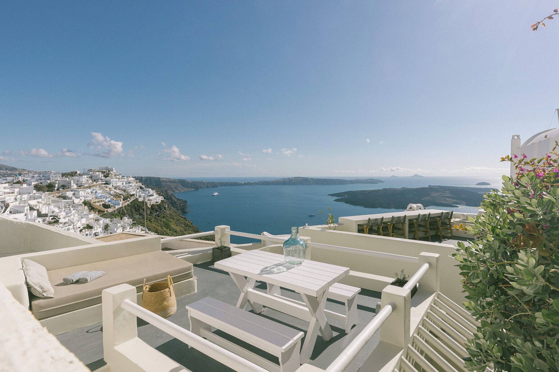A terrace with white furniture overlooking a coastal town and the sea.
