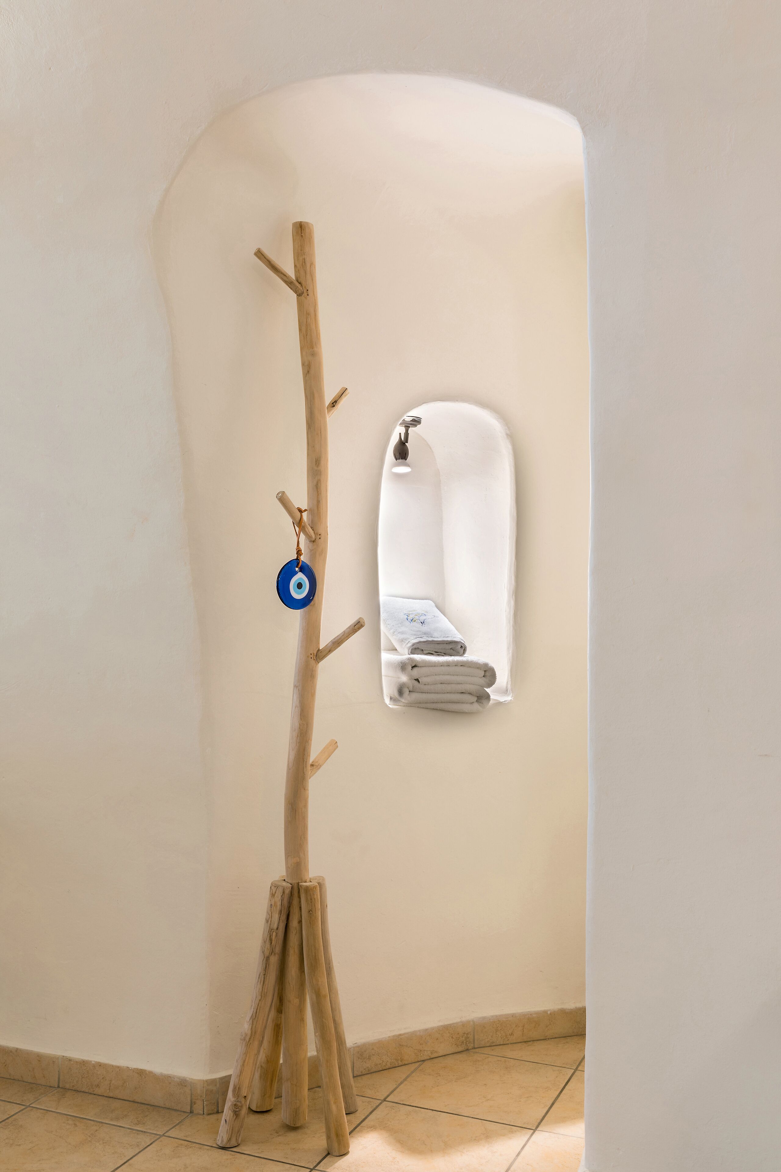 A wooden coat rack with a blue ornament, a mirror, and a towel rack against a curved wall.