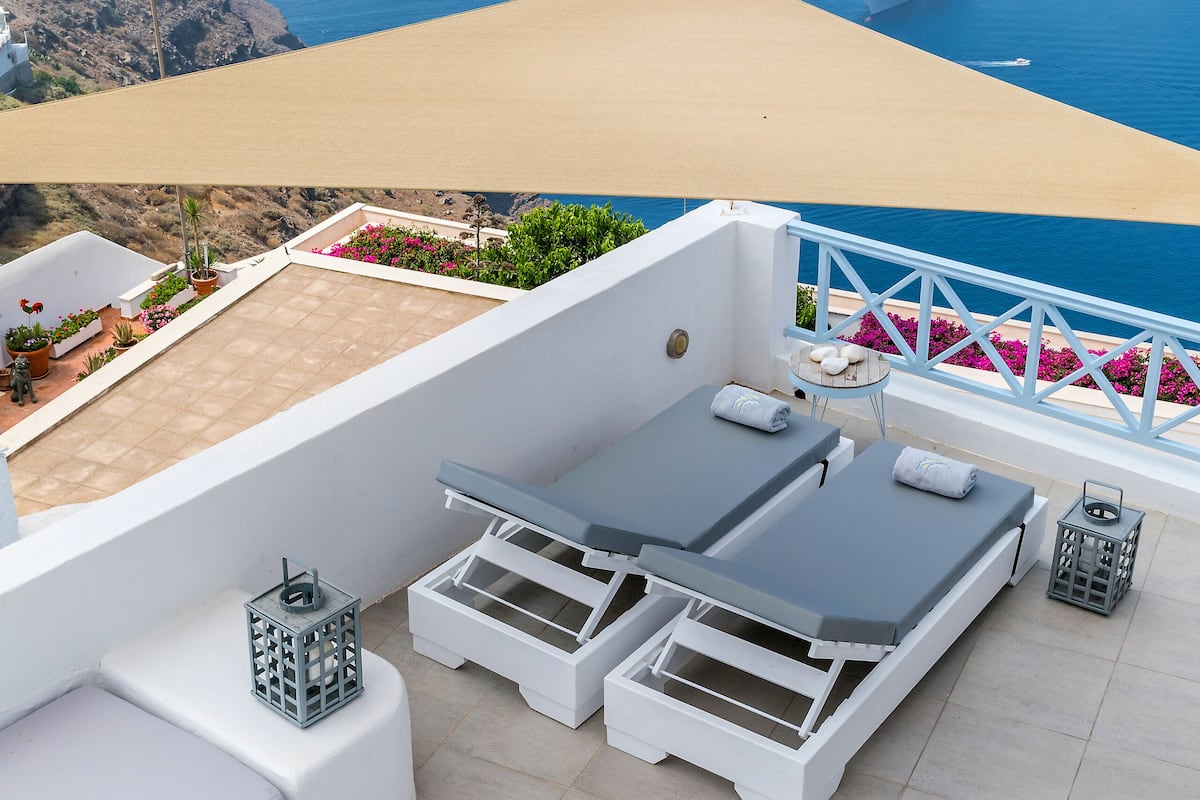 Terraço no telhado com piscina, espreguiçadeiras e vista para o mar com navios de cruzeiro.