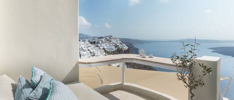 A balcony with a view of a coastal landscape, a potted plant, and a bed with pillows.