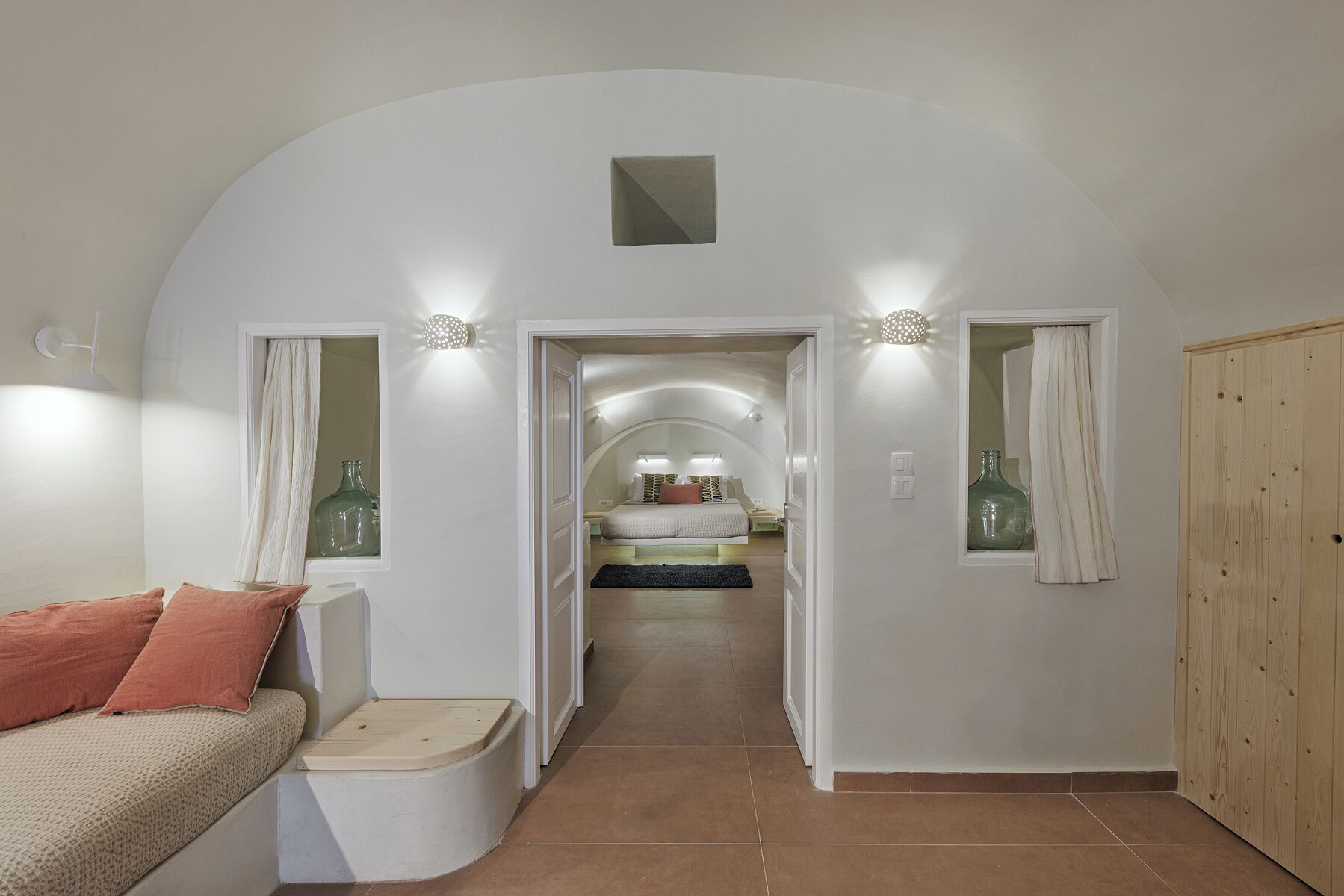 A bedroom with a curved ceiling, a bed, a nightstand, a dresser, and a wooden wardrobe.
