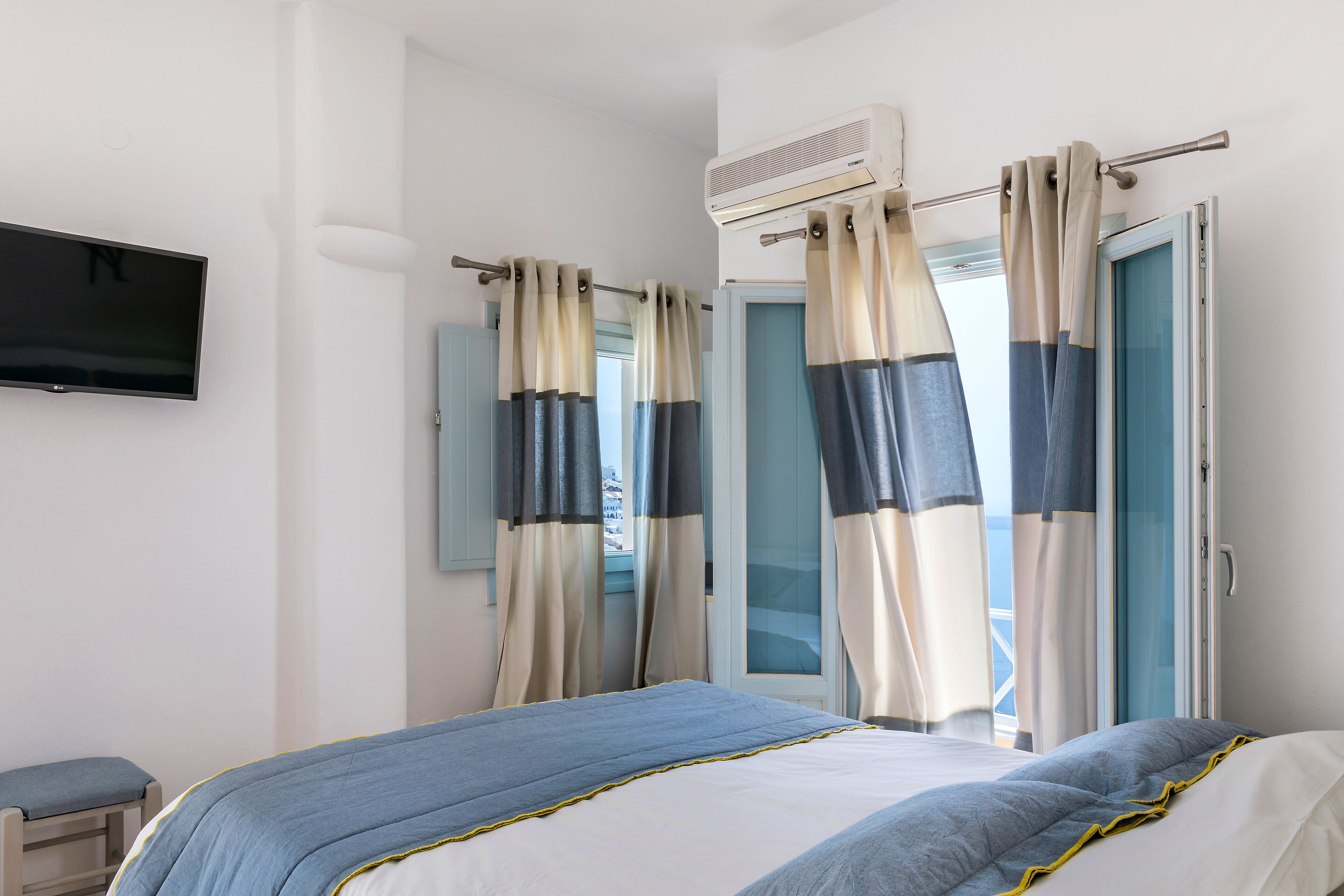 A hotel room with a bed, a TV, curtains, and an air conditioning unit.